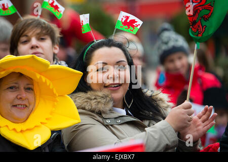 Sorridenti persone che indossano e agitando il drago rosso welsh bandiere nazionali bandiere prendendo parte al giorno di San Davide parata e celebrazioni, Wrexham, 1 marzo 2015 Foto Stock
