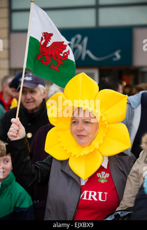 Una donna che indossa un giallo daffodil hat cofano testiera sventolare un drago rosso bandiera gallese prendendo parte al giorno di San Davide parata e celebrazioni, Wrexham, 1 marzo 2015 Foto Stock