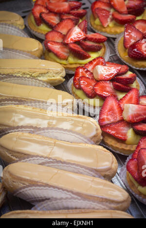 Éclairs con caffè e fragola canapes visualizzato nel negozio di dolci finestra (Francia). Éclairs au café et tartelettes aux fraises. Foto Stock