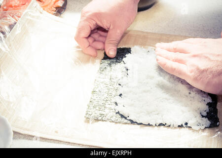 Sushi ingredienti, nori alghe makisu sul tappetino di bambù per  laminazione, crudo fresco salmone, materie di riso sushi, la salsa di soia  e bacchette sul lato Foto stock - Alamy