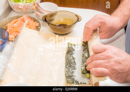 Le mani la cottura di sushi con riso, salmone e nori Foto Stock