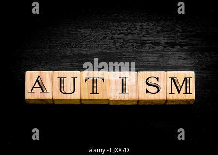 Parola autismo. Legno cubetti di piccole dimensioni con lettere isolati su sfondo nero.Concetto di immagine. Foto Stock