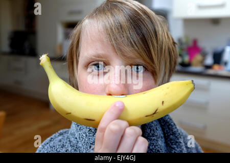 Un bambino tiene una banana pronto per fare un succo verde smoothie per una sana prima colazione Foto Stock