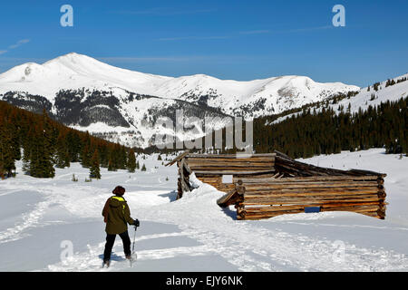 Coperte di neve Jacque picco e snowshoer a rovinato log cabin, miniera di Boston, Mayflower Gulch, vicino alla Montagna di Rame, Colorado, STATI UNITI D'AMERICA Foto Stock