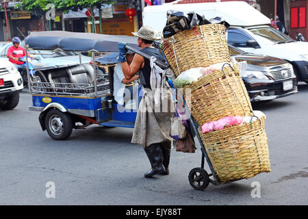 Lavoratore che trasportano i panieri di produrre in strada a Chinatown a Bangkok, in Thailandia Foto Stock