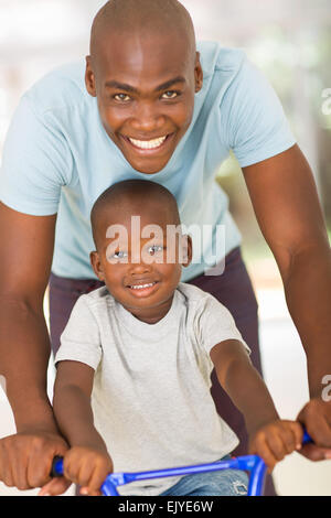 Caring giovane africano padre figlio di spinta su una bici Foto Stock