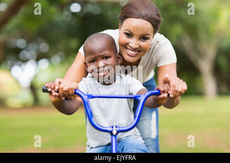 Allegro madre aiutando il suo grazioso figlio andare in bicicletta all'aperto Foto Stock