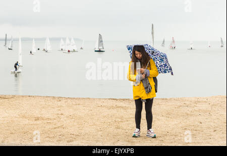 Whitstable, Regno Unito. 3 Aprile 2015: una donna stessa protegge dalle intemperie mentre utilizzando il suo telefono e Whitstable yacht club godono di una giornata sull'acqua nonostante la bank holiday pioggia. Credito: CBCK-Christine/Alamy Live News Foto Stock