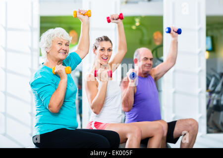 Senior l uomo e la donna con un allenatore di fitness in palestra sollevando barbells come esercizio di sport Foto Stock