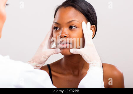 Medico donna pelle facendo controllare sul giovane donna africana prima di chirurgia estetica Foto Stock