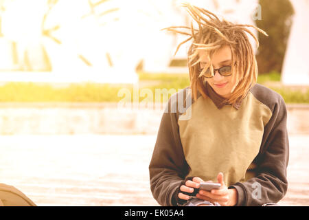 Ritratto di uno stile di vita di un giovane uomo che utilizza una smart phone all'aperto toni caldi filtro applicato Foto Stock