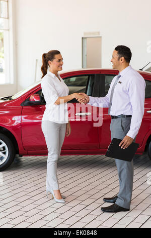 Attraente giovane donna con handshake venditore auto in showroom Foto Stock