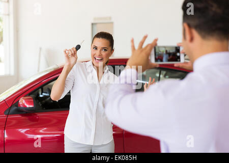 Venditore di scattare una foto del Excited donna accanto alla sua nuova vettura in showroom Foto Stock