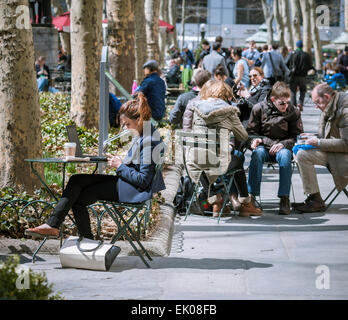 I Newyorkesi e i visitatori utilizzano i loro dispositivi elettronici che hanno versato la malinconia invernale in Bryant Park di New York il giovedì, 2 aprile 2015. Clima caldo nei metà di anni sessanta ha attratto gli impiegati e i turisti all'esterno. (© Richard B. Levine) Foto Stock