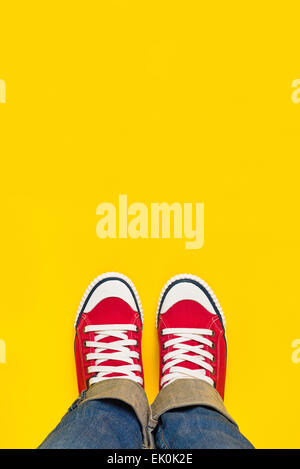 Piedi dal concetto di cui sopra, persona adolescente in rosso Sneakers in piedi su sfondo giallo, B;lank copia spazio nella parte anteriore. Foto Stock