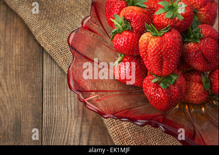 Fresche fragole mature in recipiente di vetro su sfondo di legno. Primo piano. Foto Stock
