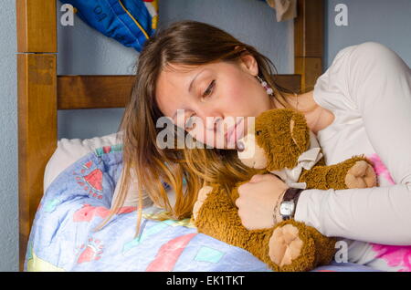 Ragazza triste abbracciando il suo giocattolo recare sul letto Foto Stock