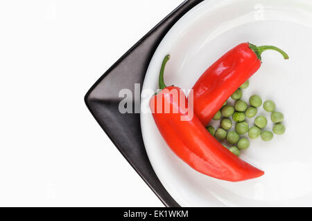 Peperoni rossi e piselli su bianco e la piastra nera Foto Stock