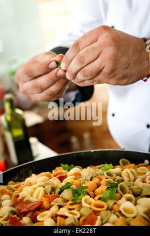 Fatto a mano le orecchiette o 'piccole orecchie' di pasta in un rustico di salsa di pomodoro con parmigiano grattugiato guarnita con un ciuffo di basilico fresco Foto Stock