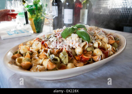 Fatto a mano le orecchiette o 'piccole orecchie' di pasta in un rustico di salsa di pomodoro con parmigiano grattugiato guarnita con un ciuffo di basilico fresco Foto Stock