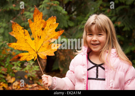 4 anno vecchia ragazza gioca con una grande foglia foglia di acero, mostrando come è grande in confronto alla sua testa Foto Stock