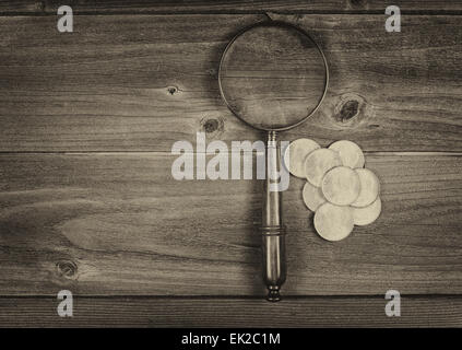 Concetto di vintage di un antico round a forma di lente di ingrandimento e di una pila di vecchi silver dollar monete sul legno rustico Foto Stock