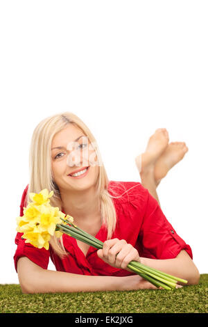 Colpo verticale di una giovane donna bionda tenendo un mazzo di tulipani gialli e giacente su di una superficie di erba Foto Stock