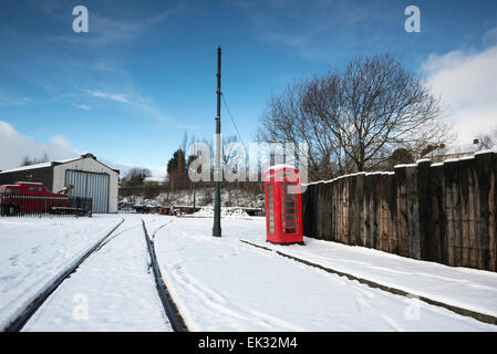 Telefono rosso scatola sulla coperta di neve strada in Summerlee museo del patrimonio industriale. Ferrovia linee del tram attraverso la neve. . Foto Stock