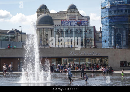 Bradford, West Yorkshire, Regno Unito, 6 aprile 2015. Adulti e bambini e adolescenti godere la città parco piscina a specchio e fontane in Centenary Square, il più grande del Regno Unito, centro città d'acqua. Il Pavillion Cafe e il Teatro Alhambra in background. Un felice mix multiculturale di persone o canoa, bagni di sole e di divertimento su una soleggiata Pasqua lunedì festivo. Credito: Mick Flynn/Alamy Live News Foto Stock