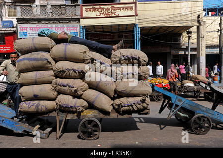 Lavoratore dormendo su una pila di sacchi di riso nel mezzo di un affollato mercato a Delhi, India Foto Stock