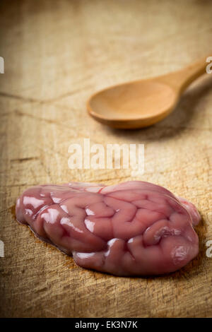 Cervello di maiale su uno sfondo di legno con il cucchiaio di legno Foto Stock