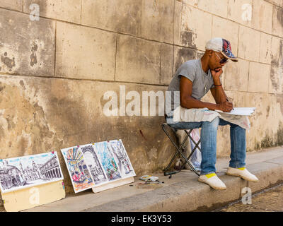 Un artista afro-cubane si siede e schizzi mentre egli mostra i suoi dipinti in vendita da li pendente contro un muro di pietra a l'Avana. Foto Stock