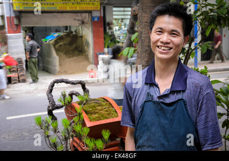 L'uomo in Cina vendita penzai in miniatura (altrimenti noto come penjing) alberi, la versione cinese del bonsai. Pressione di stallo di strada, Guangzhou, giovane venditore; Foto Stock