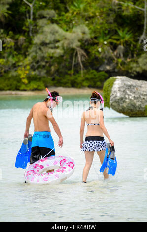 Una giovane coppia giapponese immettere l'acqua a una spiaggia tropicale, pronto a fare snorkeling; giapponese di turisti internazionali; turismo; Sud Pacifico; Nuova Caledonia Foto Stock