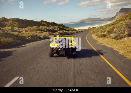 Vista posteriore coppia giovane guida in un piccolo scoperto veicolo. Amore matura sul viaggio in spiaggia in buggy car. Foto Stock