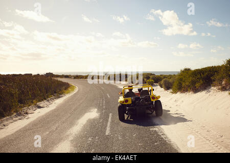 Vista posteriore della coppia giovane guida lungo una strada aperta per la spiaggia in una giornata di sole. Coppia in viaggio su strada in una piccola spiaggia in buggy car. Foto Stock