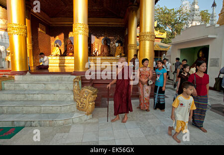 Un vecchio monaco buddista e famiglie a piedi intorno alla Shwedagon pagoda come il sole tramonta in Yangon Myanmar Foto Stock