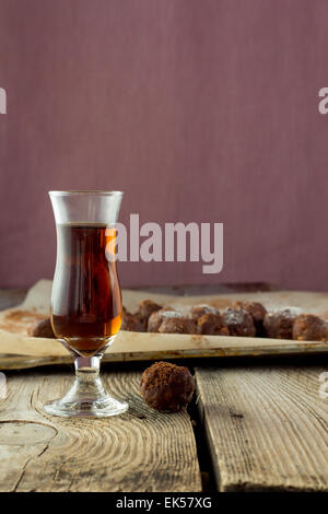 Piccolo bicchiere di liquore e caramelle fatte in casa sul tavolo di legno Foto Stock