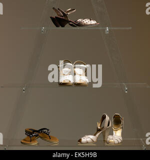 Selezione di scarpe da donna disposte su ripiani in vetro trasparente su uno sfondo neutro, che presentano diversi stili, tra cui il tacco alto Foto Stock