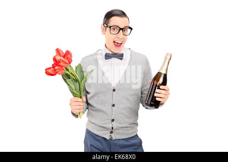 Eccitato giovane tenendo un mazzo di tulipani rossi e una bottiglia di champagne isolato su sfondo bianco Foto Stock