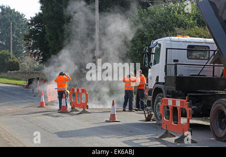 Operai posa di nuovo asfalto durante l'installazione di nuovo a banda larga ad alta velocità i cavi a fibre ottiche in un territorio rurale Oxfordshire village Foto Stock