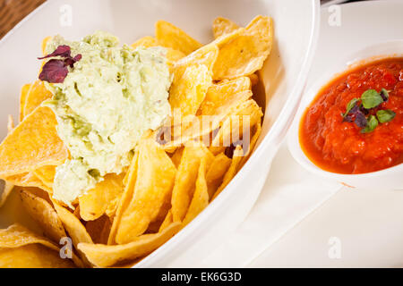 Mais fresco nachos con fresca piccante salsa guacamole e un rabbocco d'avocado servito come uno spuntino o un aperitivo in una ciotola bianco Foto Stock
