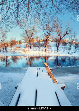 Bel ponte con acqua, neve, cielo blu e rami. Tramonto in inverno presso il fiume Krinka. Foresta in Ucraina Foto Stock