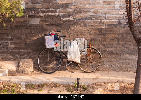 Vecchia bicicletta è appoggiata contro il vecchio muro di mattoni. Foto Stock