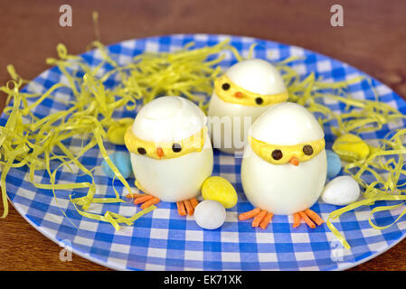 Pasqua uova deviled pulcini con la caramella e uova erba giallo su blu e bianco piastra a scacchi. Foto Stock