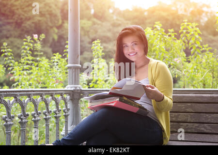 Bellissima femmina giovane studente universitario con libri e file sul giro, seduti su una panca di legno sotto la pergola in un parco. Foto Stock