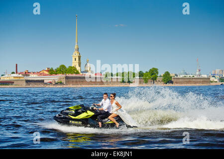 Sposi novelli vai su jet sci, la sposa e lo sposo sullo sfondo della fortezza di Pietro e Paolo, la zona di acqua del fiume Neva Foto Stock