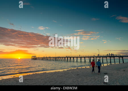 Una giovane coppia sta camminando lungo la spiaggia al tramonto e tenendo le mani Foto Stock