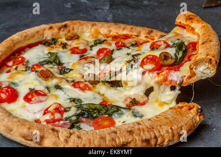 Una vista ravvicinata di una casa fatta di crosta sottile trancio di pizza con Olive Pomodori Peperoni basilico mozzarella, London REGNO UNITO Foto Stock