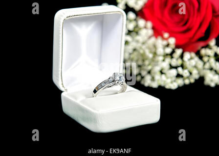 Anello di diamante nella casella bianca con rosa rossa su nero. Foto Stock